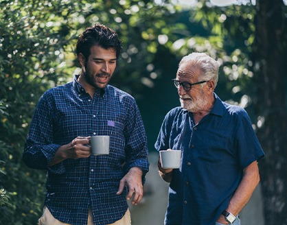 Older and younger man walking and talking outside with mugs