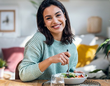 Woman in green sweater at table eating salad