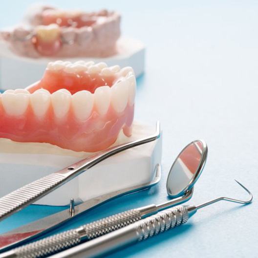 Close up of a lower denture next to several dental tools