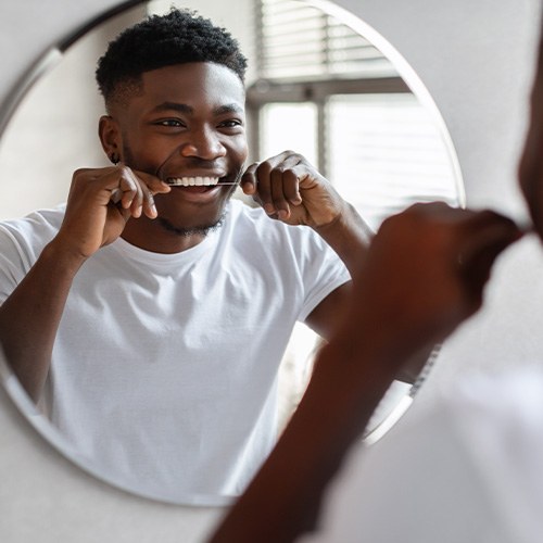 Man smiling while flossing in bathroom