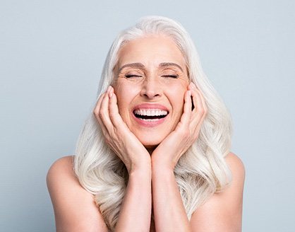 Woman with white hair smiling holding hands to cheeks