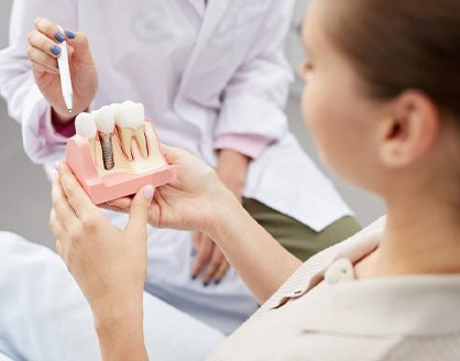 Dentist pointing out a dental implant in a model while patient listens