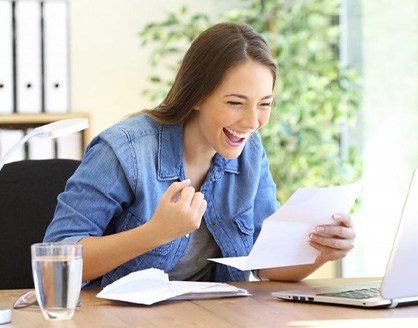 Woman celebrating at her desk after reviewing dental insurance policy
