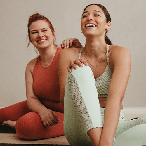 Two friends smiling while sitting in workout studio