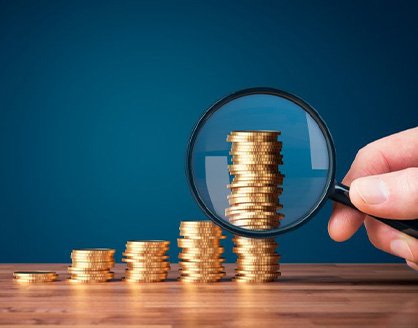 Hand holding a magnifying glass to inspect a stack of coins