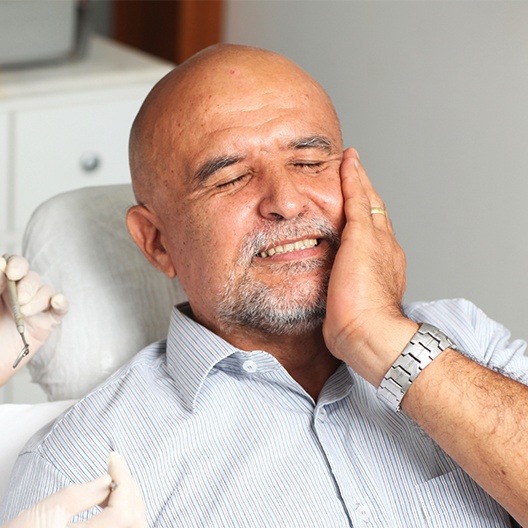 Man in need of emergency dentistry holding cheek in pain