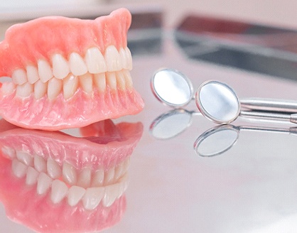 full dentures sitting next to two dental mirrors on a countertop