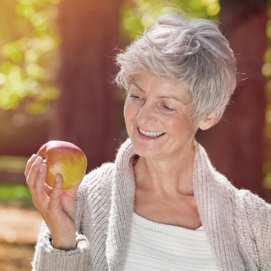 Smiling woman eating an apple after dental implant tooth replacement