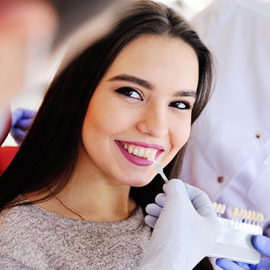 Woman smiling while dentist matches veneer shades