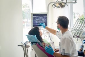 Woman in flowered shirt in dental chair looking at an X-ray of her teeth with a dentist in blue gloves